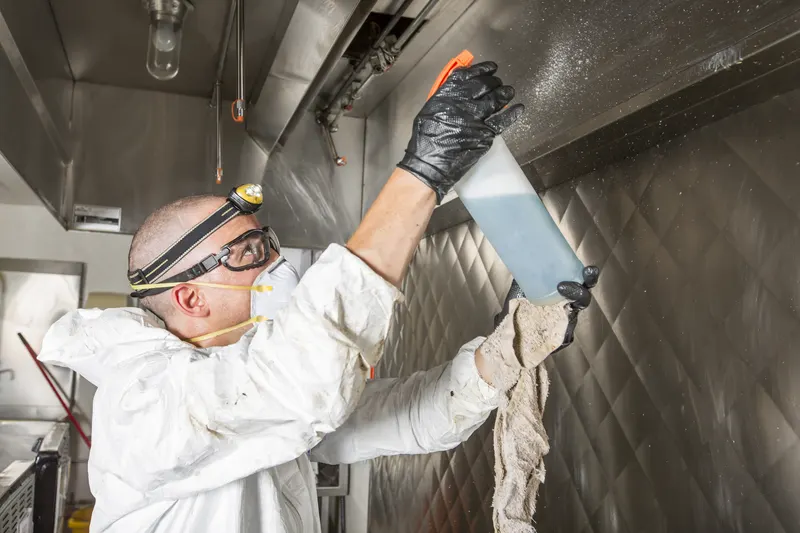 Overhead view of a technician spraying degreaser across the interior of a stainless steel exhaust canopy