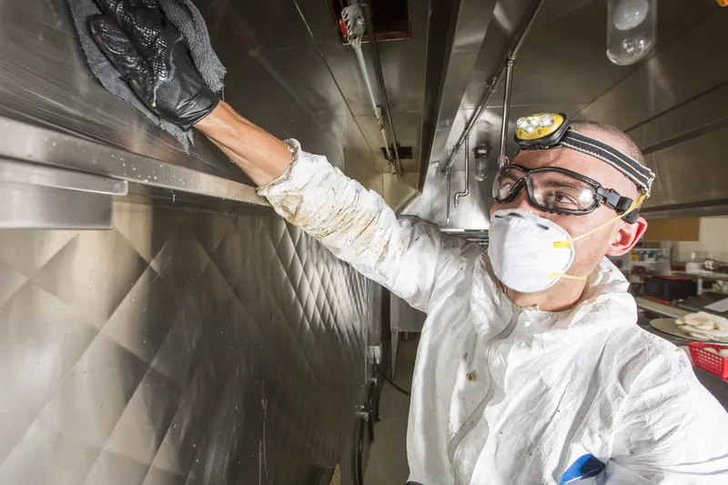 Technician reaching into the plenum behind a removed baffle filter in a commercial kitchen hood