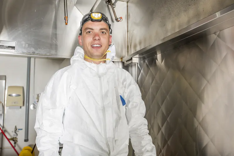Technician in protective gloves lifting a stainless steel baffle filter out of the slot at the back of a wall canopy hood