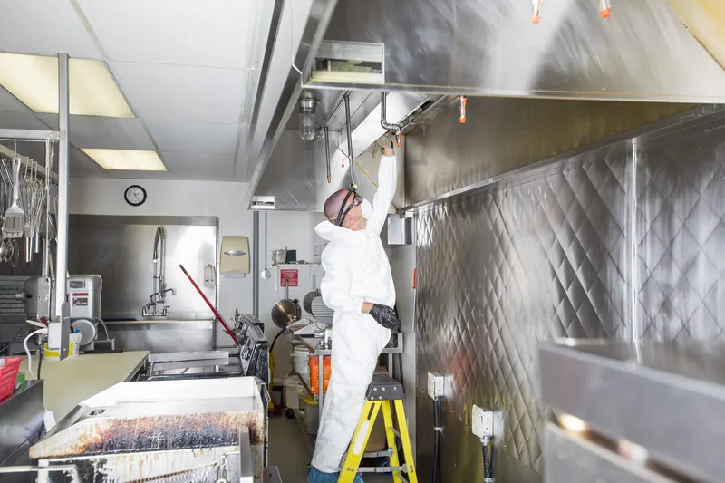 Step ladder set up under a commercial kitchen exhaust hood with cleaning equipment laid out on a covered stainless steel prep table